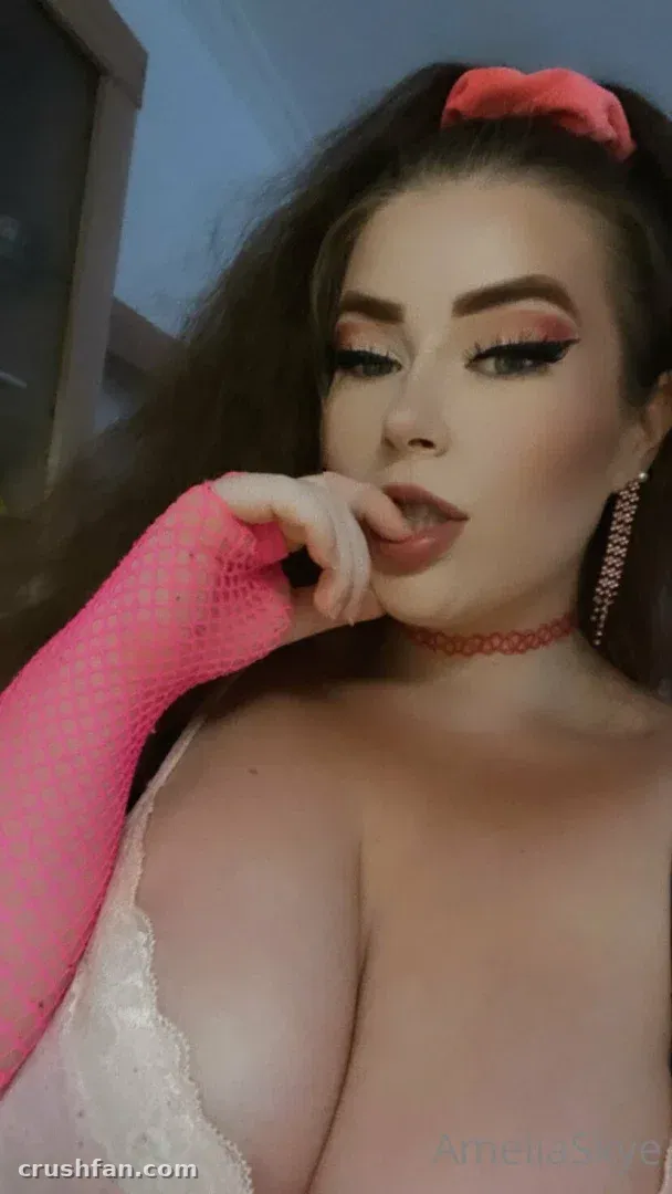 Retrato em close de Amelia Skye com luvas de rede rosa, um top de renda e uma gargantilha vermelha