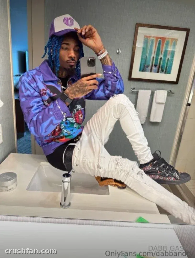DABB LAND in a purple jacket and white pants taking a mirror selfie in a bathroom.