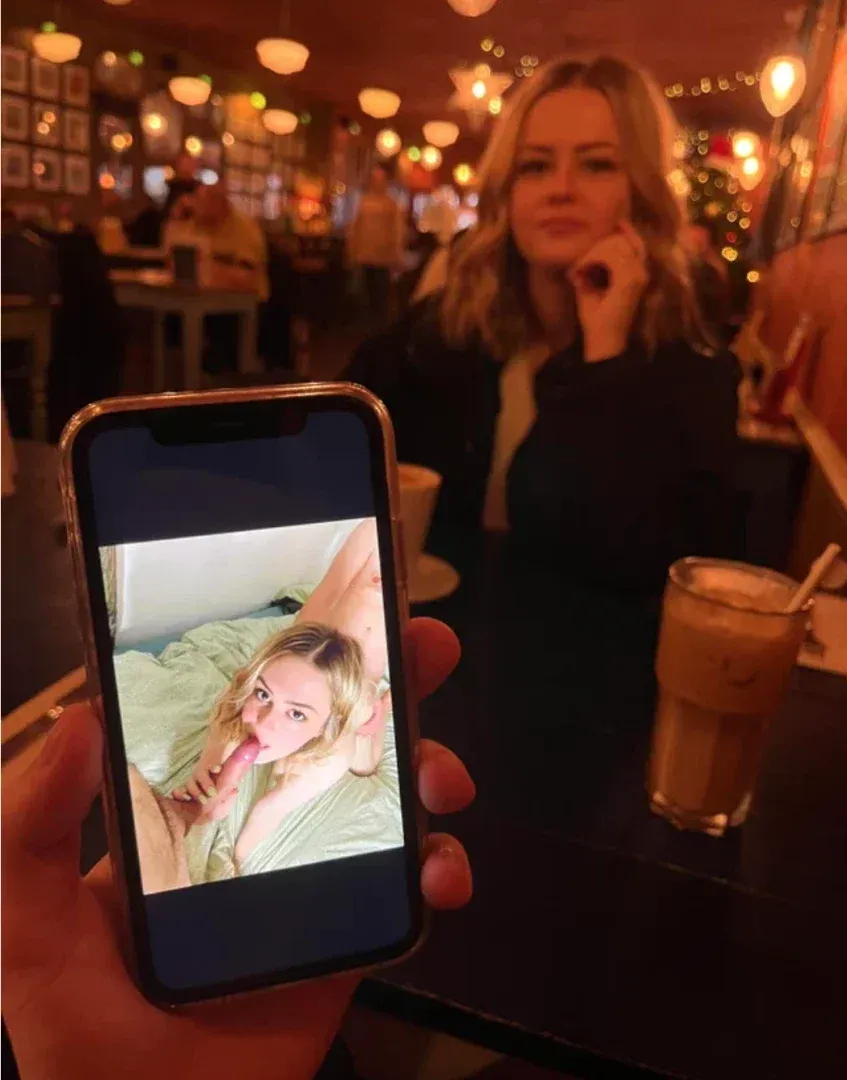 Criadora em um café aconchegante segurando um celular que mostra uma foto brilhante dela mesma.
