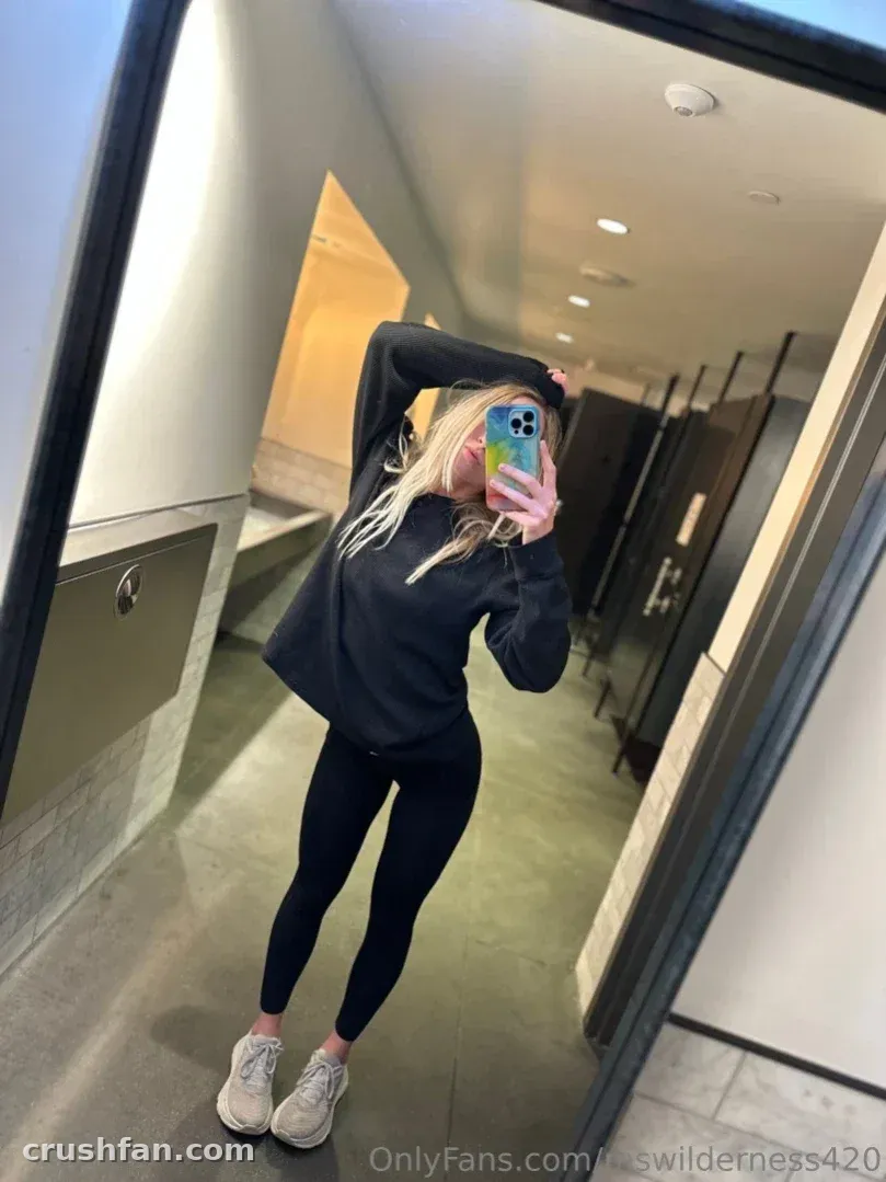 Ms Wilderness taking a mirror selfie in a black hoodie and leggings in a hallway