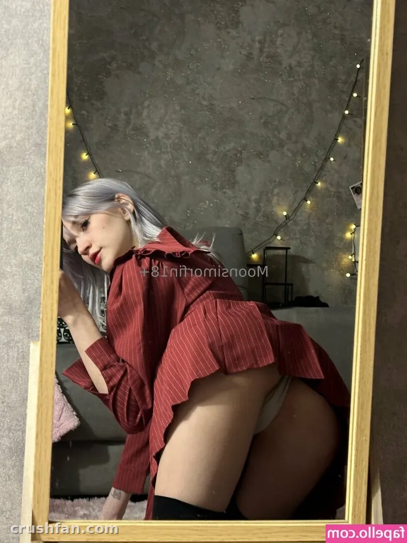La creadora Moonsi con una camisa roja de rayas finas posando frente a un espejo con luces detrás de ella.
