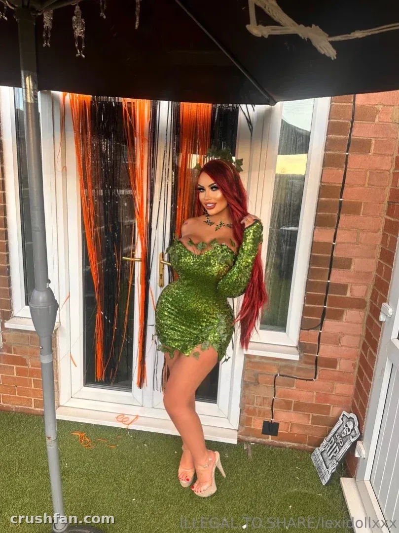 Lexi dans un costume à sequins verts posant sur du gazon artificiel près d'un mur de briques et d'une décoration de guirlande