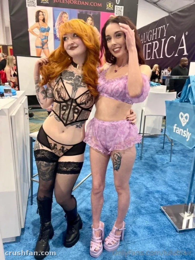 Lulu Blair en lingerie noire et bas, debout sur une moquette bleue sur un stand de convention