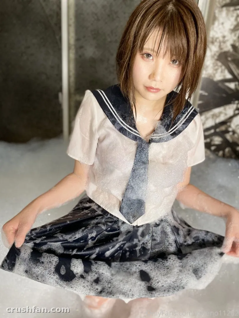Creator in a sailor-style top and dark skirt posing amid soapy foam against a textured wall.