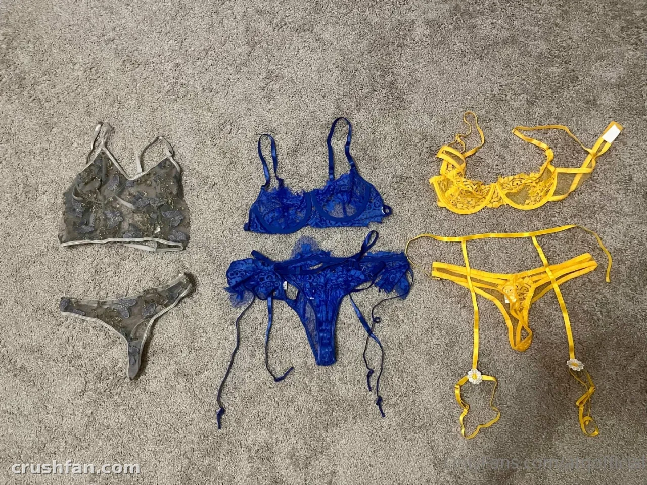 Três conjuntos de lingerie em cinza, azul e amarelo dispostos em um tapete cinza
