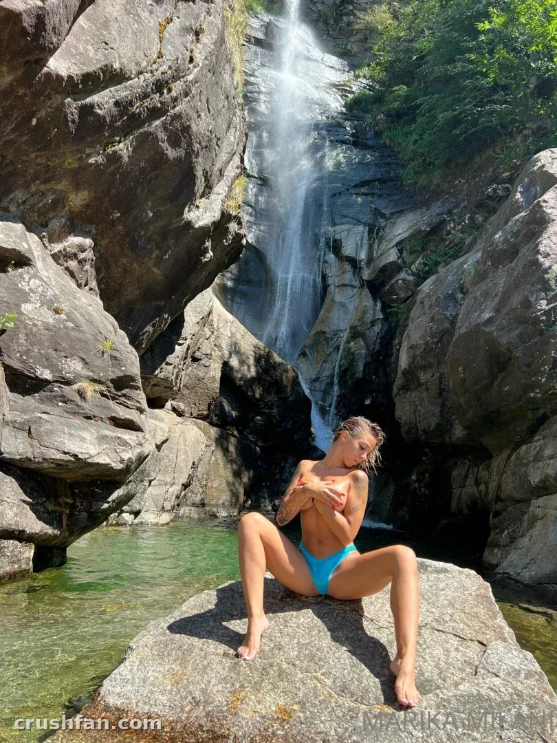 Woman in turquoise bikini sitting on a rock in front of a waterfall