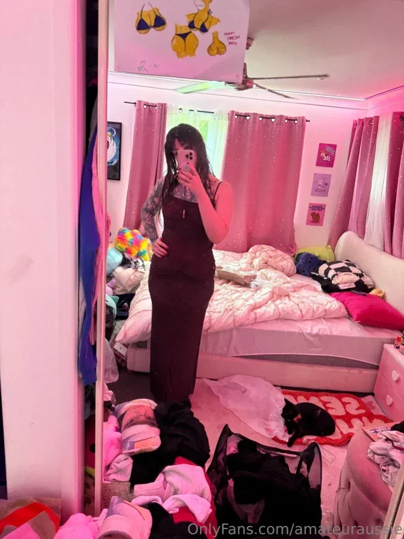 Aus Sarah dans une tenue sombre prenant un selfie dans le miroir dans une chambre éclairée en rose