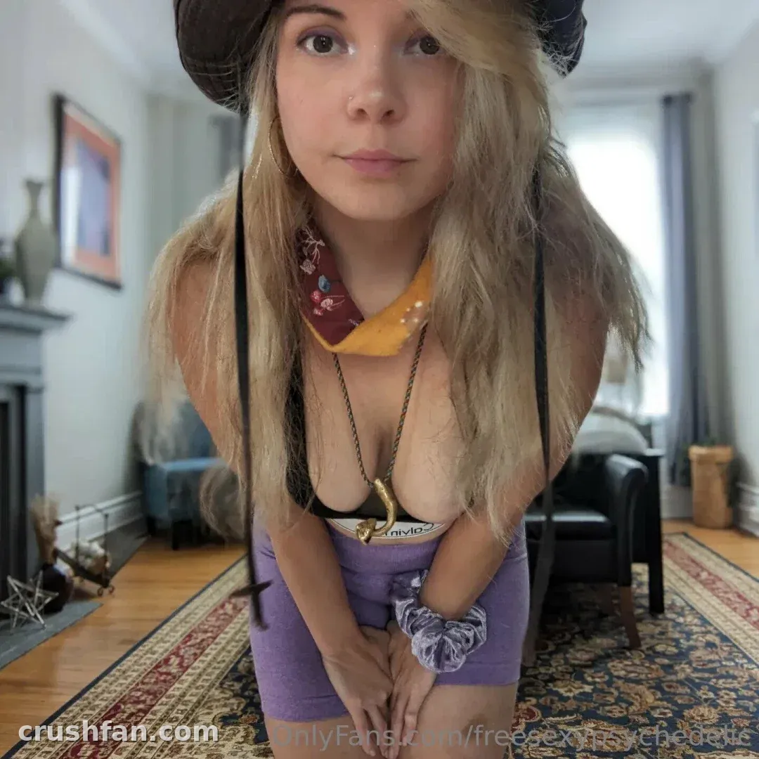 Creator in a wide-brim hat and purple skirt leaning toward the camera in a living room