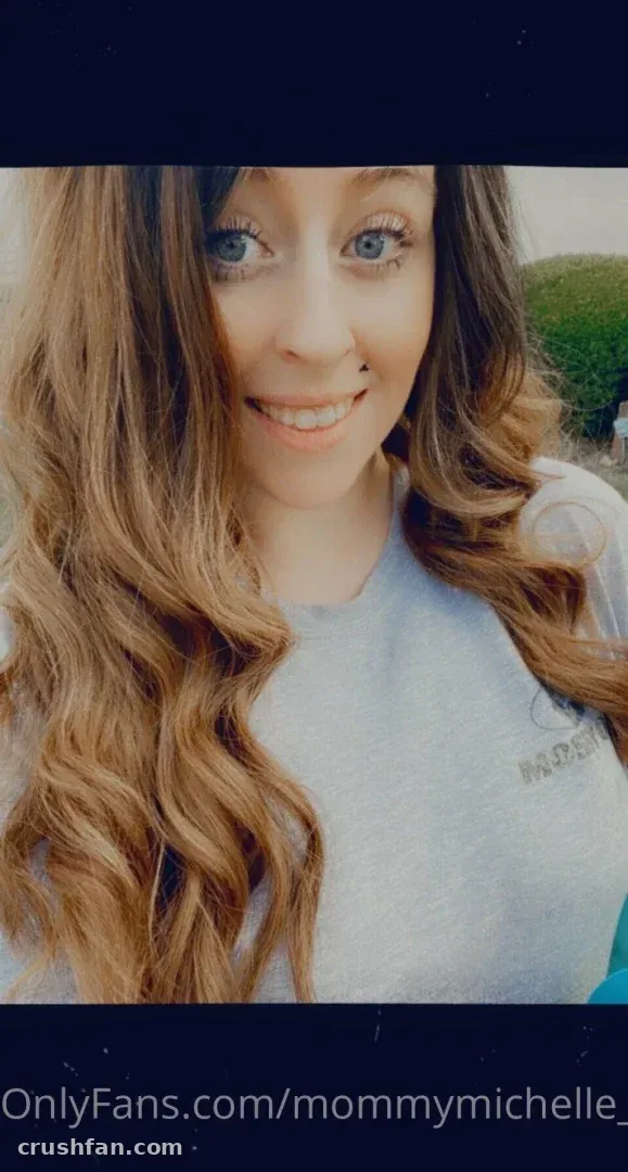 Michelle sorrindo em uma selfie em close ao ar livre usando uma blusa cinza-clara