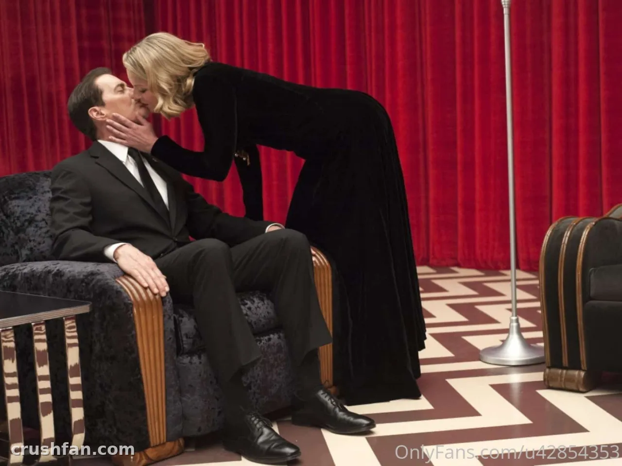 Kim in a long black gown leaning toward a seated man in a dark suit against red curtains