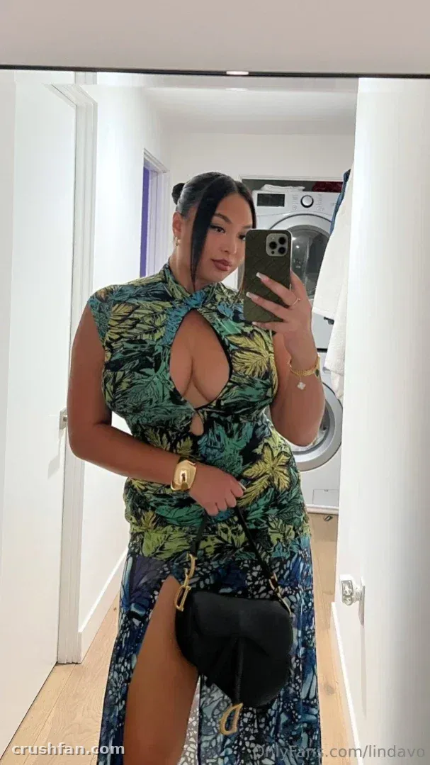 Linda Vo com um vestido verde de estampa tropical tirando uma selfie no espelho em um corredor