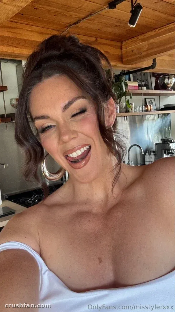 Alison Tyler laughing in a white top and hoop earrings inside a wooden kitchen.