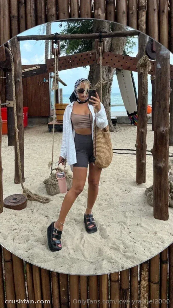 Lovely Rachel macht ein Spiegel-Selfie an einem Sandstrand mit einer Strohtasche.