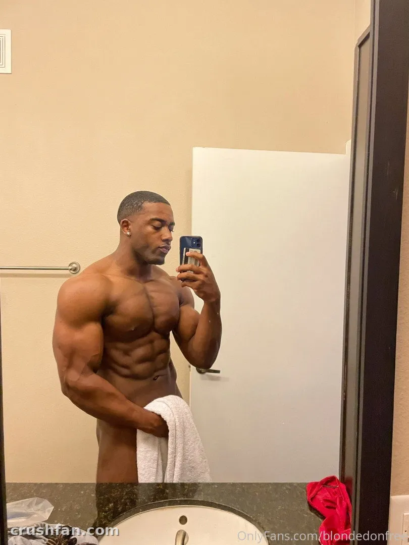 Closer Look Men Free taking a shirtless mirror selfie in a bathroom while holding a white towel.