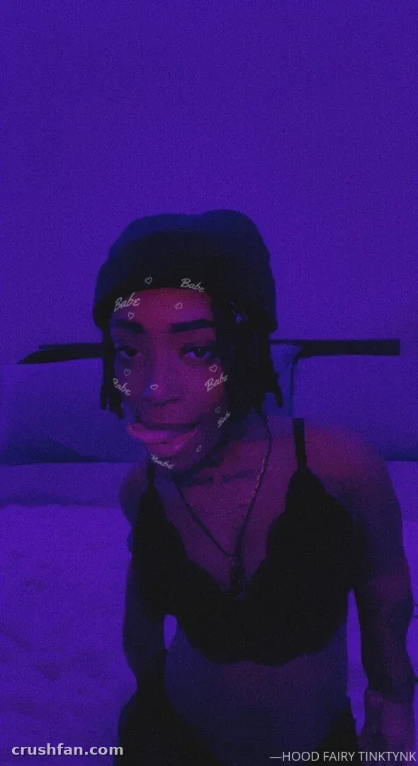 TINKY WINKY sous une lumière violette portant un bonnet et un haut sombre avec des autocollants sur le visage