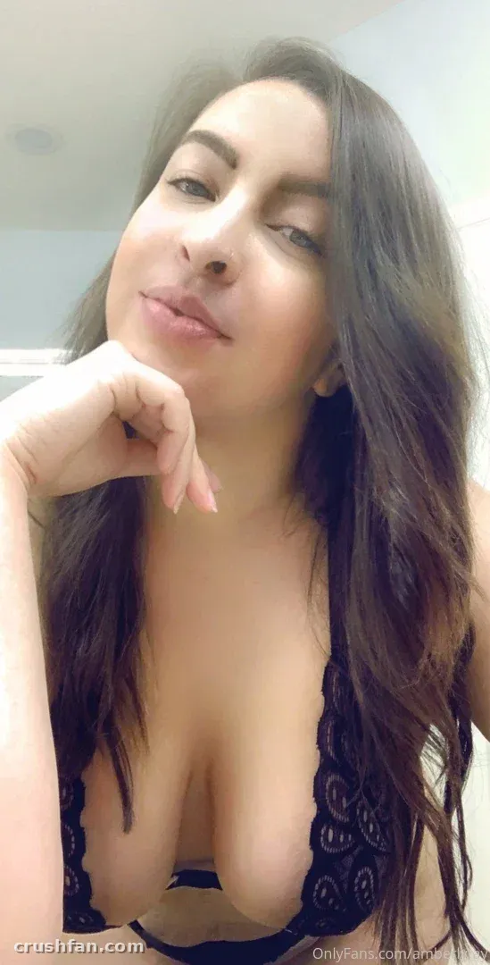 Amberly con una blusa de encaje negro apoyando la barbilla en la mano en un retrato suave de interior