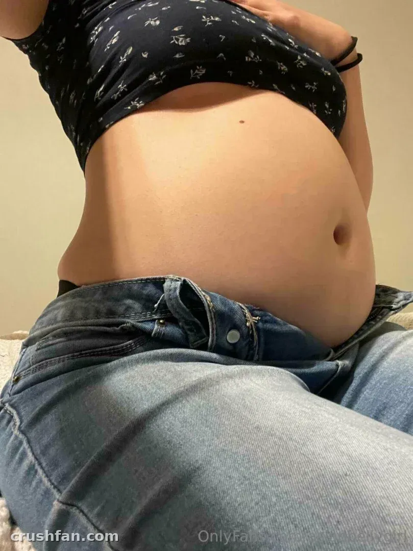 Close view of a woman lifting a dark floral crop top above light blue jeans
