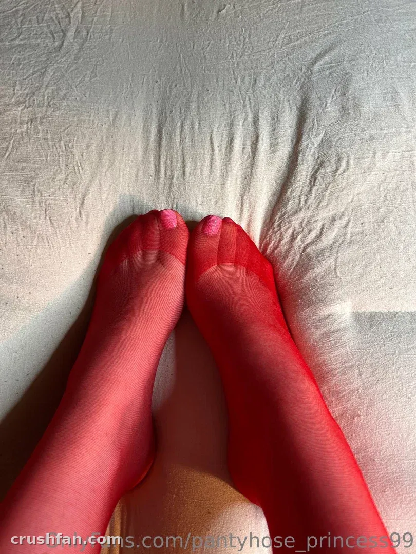 Red nylon-clad legs and pink-painted toes resting on white bed sheets