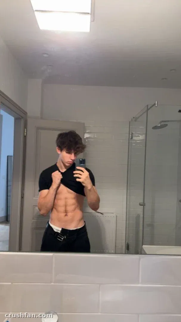 Manu lifting his black t-shirt in a bright tiled bathroom mirror selfie