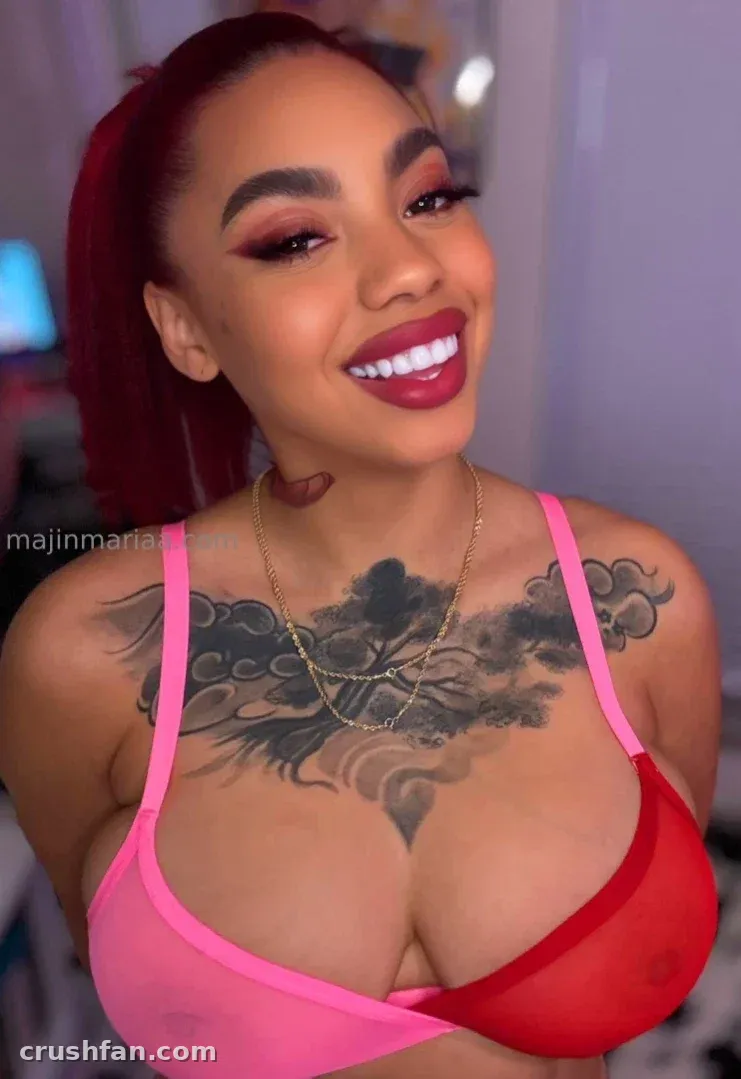 Mariaa Skyy lächelnd in einem pinken und roten Top mit einer Goldkette und einem Tattoo auf der Brust.
