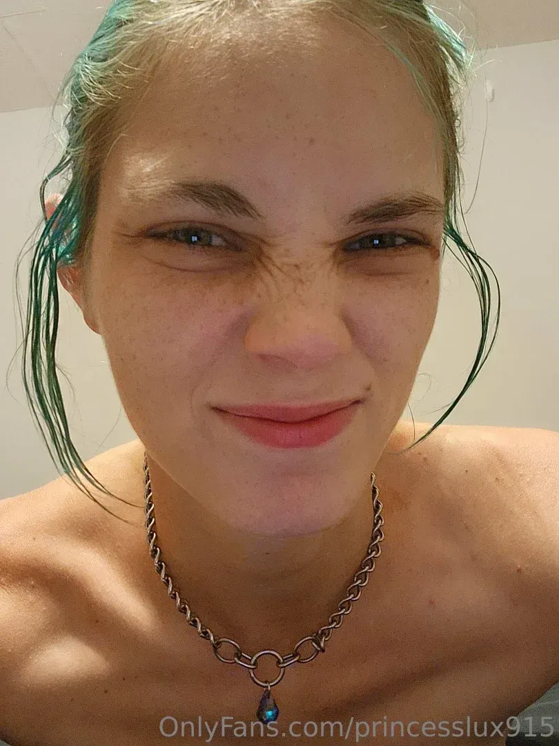Princess Lux sonriendo en un selfie en primer plano con cabello verde y un collar de plata.