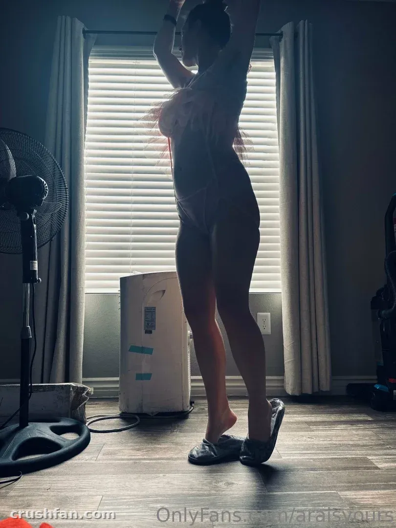 Ara steht als Silhouette mit erhobenen Armen vor einem hellen Fenster mit Jalousien.