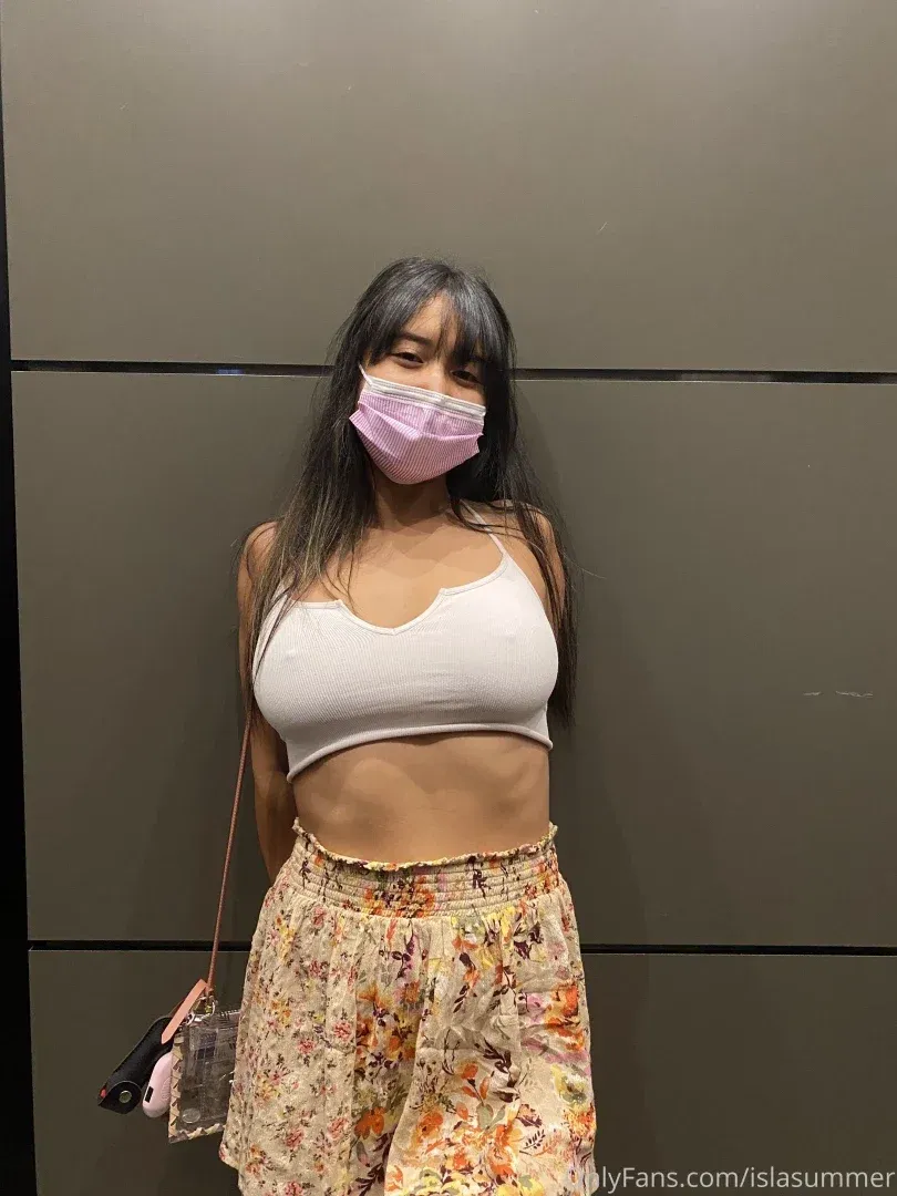 Isla Summer in a white crop top, floral skirt and pink face mask against a grey wall