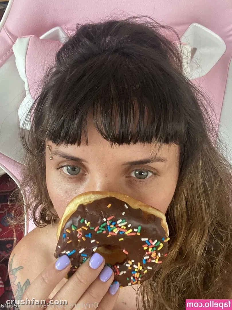 Selfie rapproché d'une femme tenant un donut au chocolat avec des pépites devant son visage