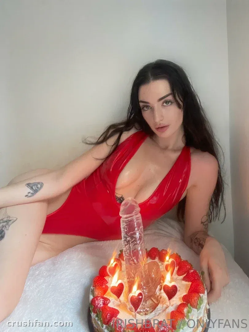 Claudia con un body de látex rojo sentada junto a una tarta de fresas con velas encendidas