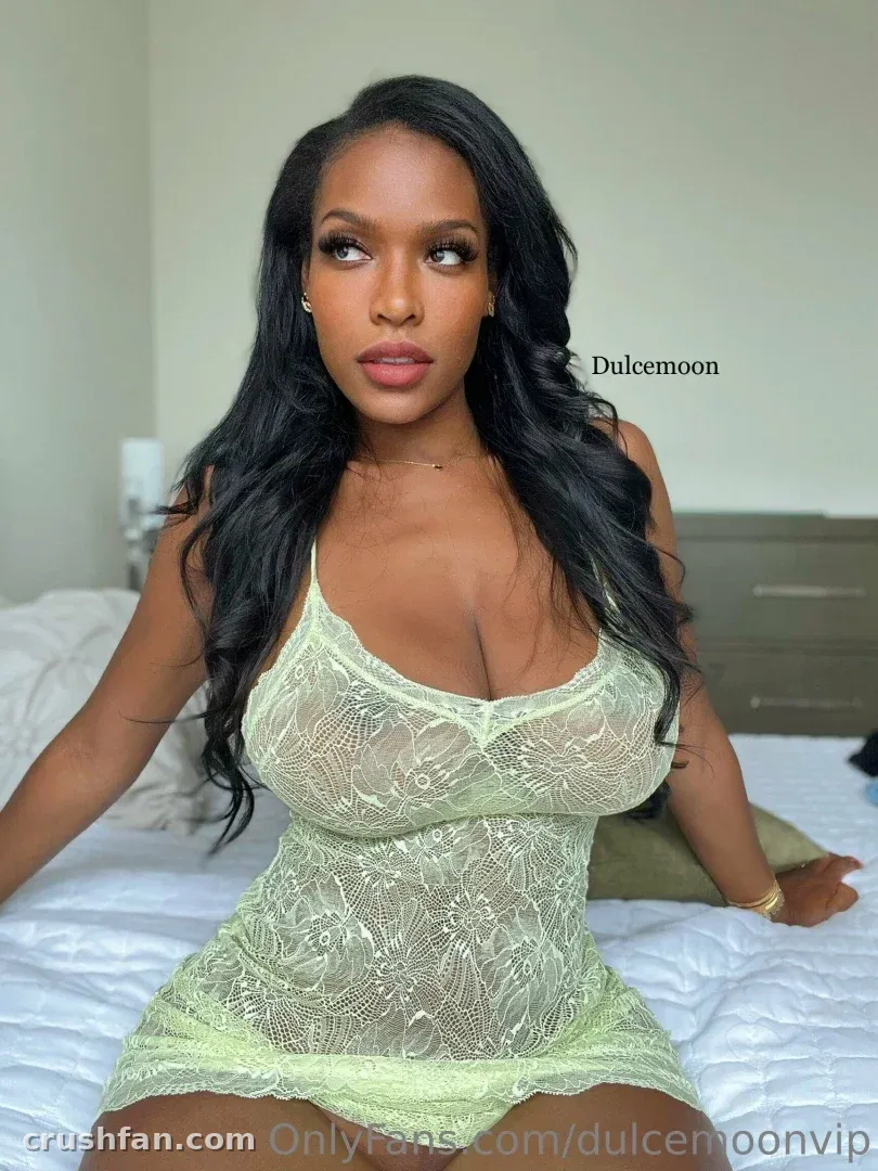 Dulcemoonvip in pale green lace lingerie seated on a white bed indoors
