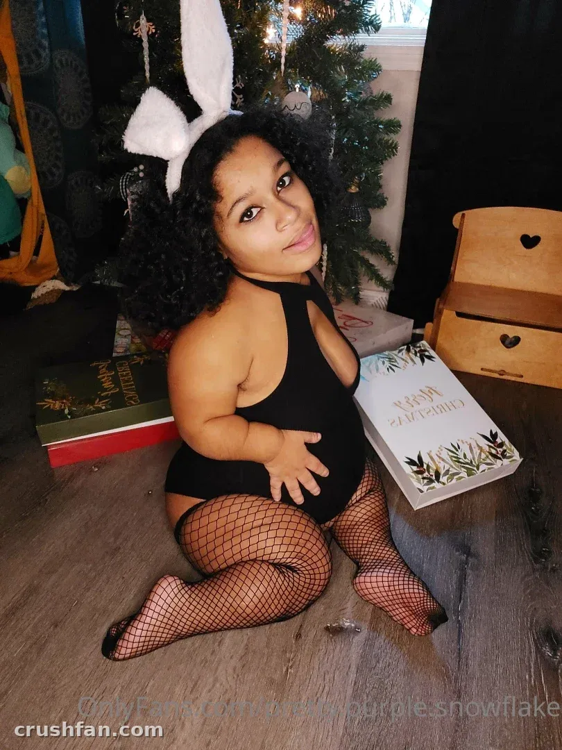 Jade in a black bodysuit and fishnet tights with bunny ears, sitting on a wooden floor near a Christmas tree.