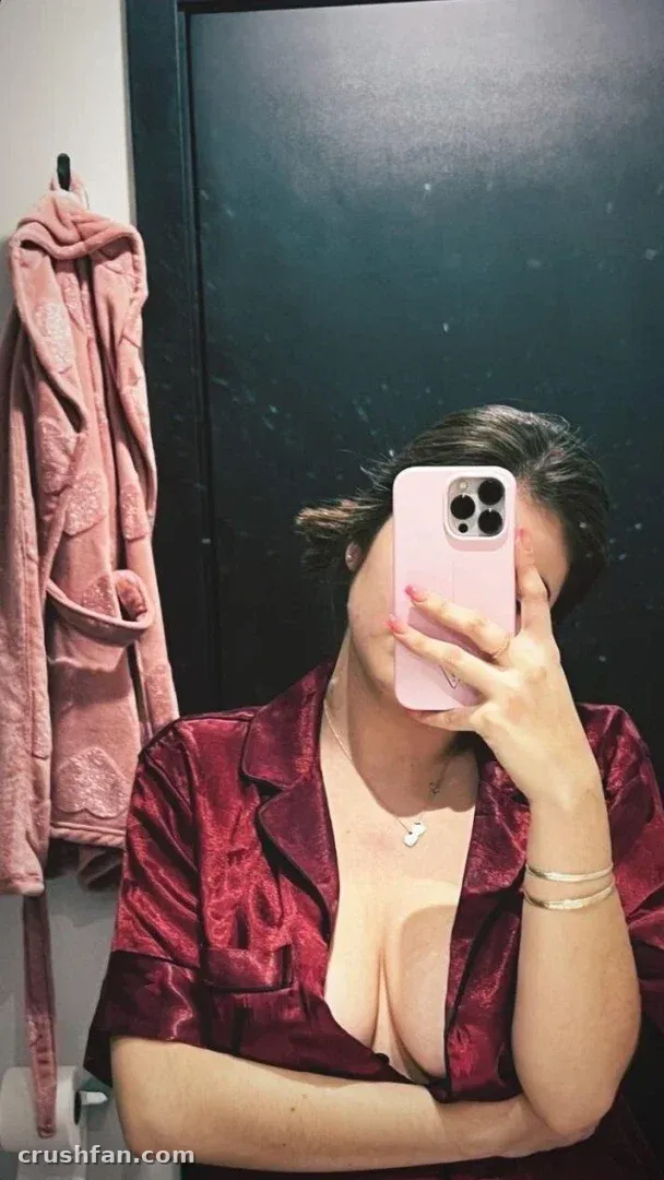 Gabrielle in a burgundy satin shirt taking a mirror selfie with a pink phone.