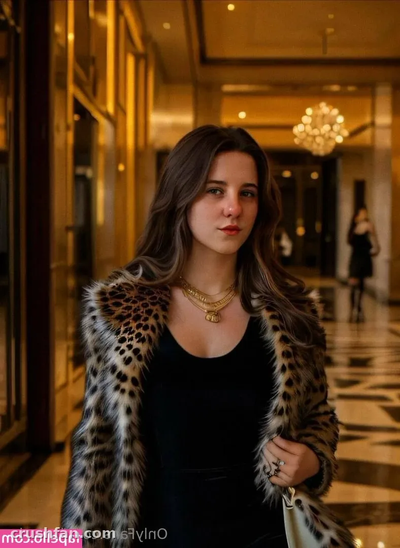Mulher com um casaco de estampa de leopardo e blusa preta em pé em um corredor de hotel com iluminação aconchegante.