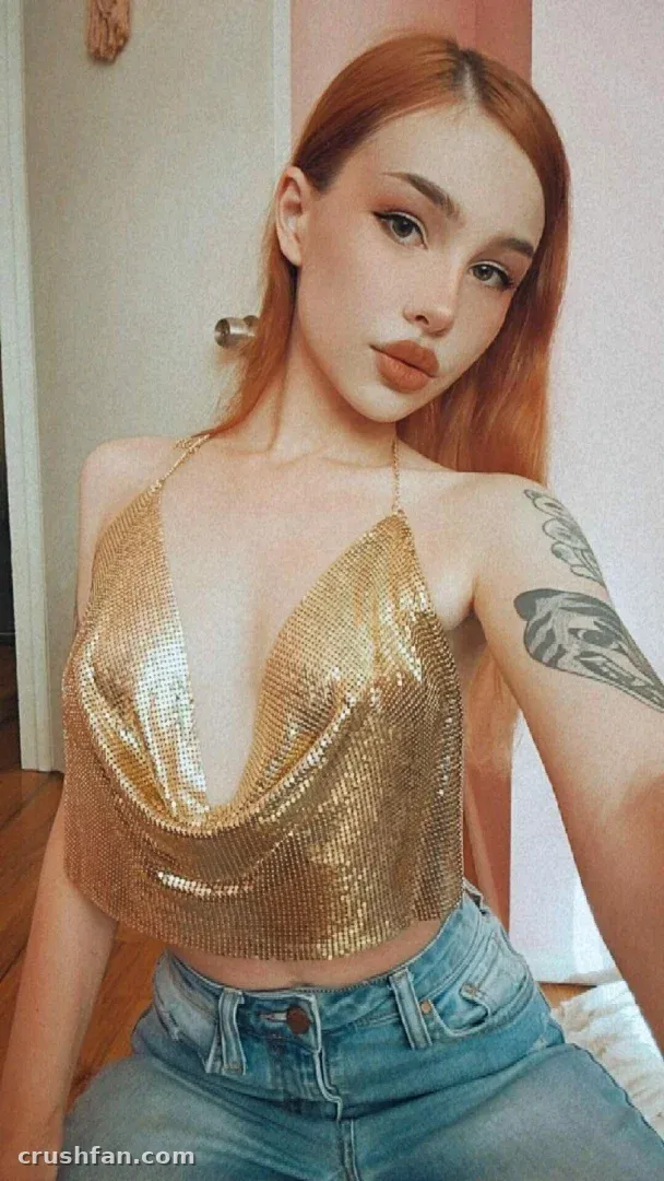 Gwen in a gold chainmail halter top and blue jeans taking an indoor selfie