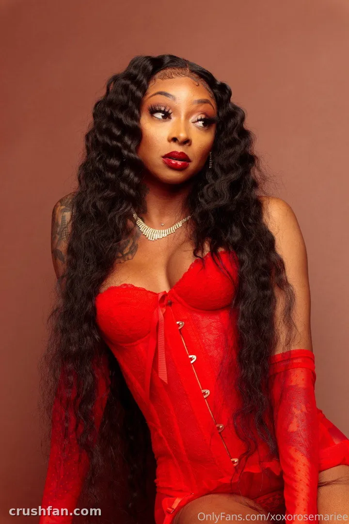 Persuasian in a red corset and long red gloves against a brown studio wall