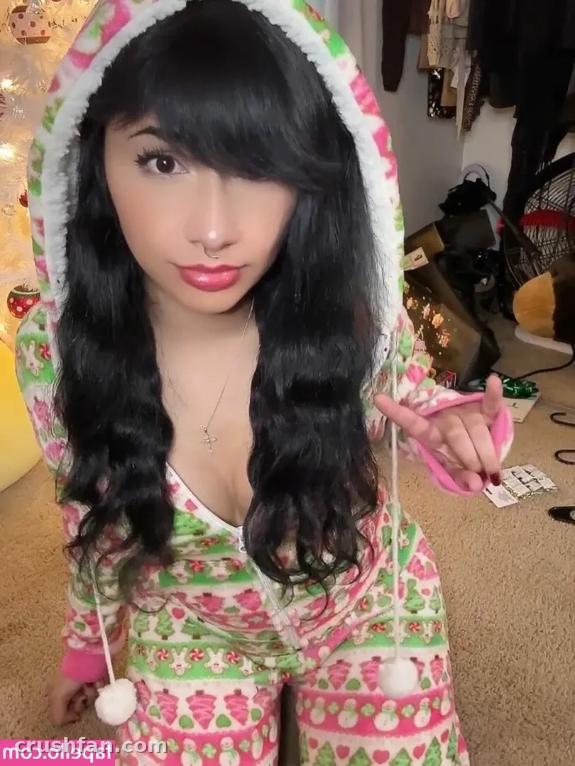 Creator in a festive pink and green hooded outfit posing indoors with one hand raised