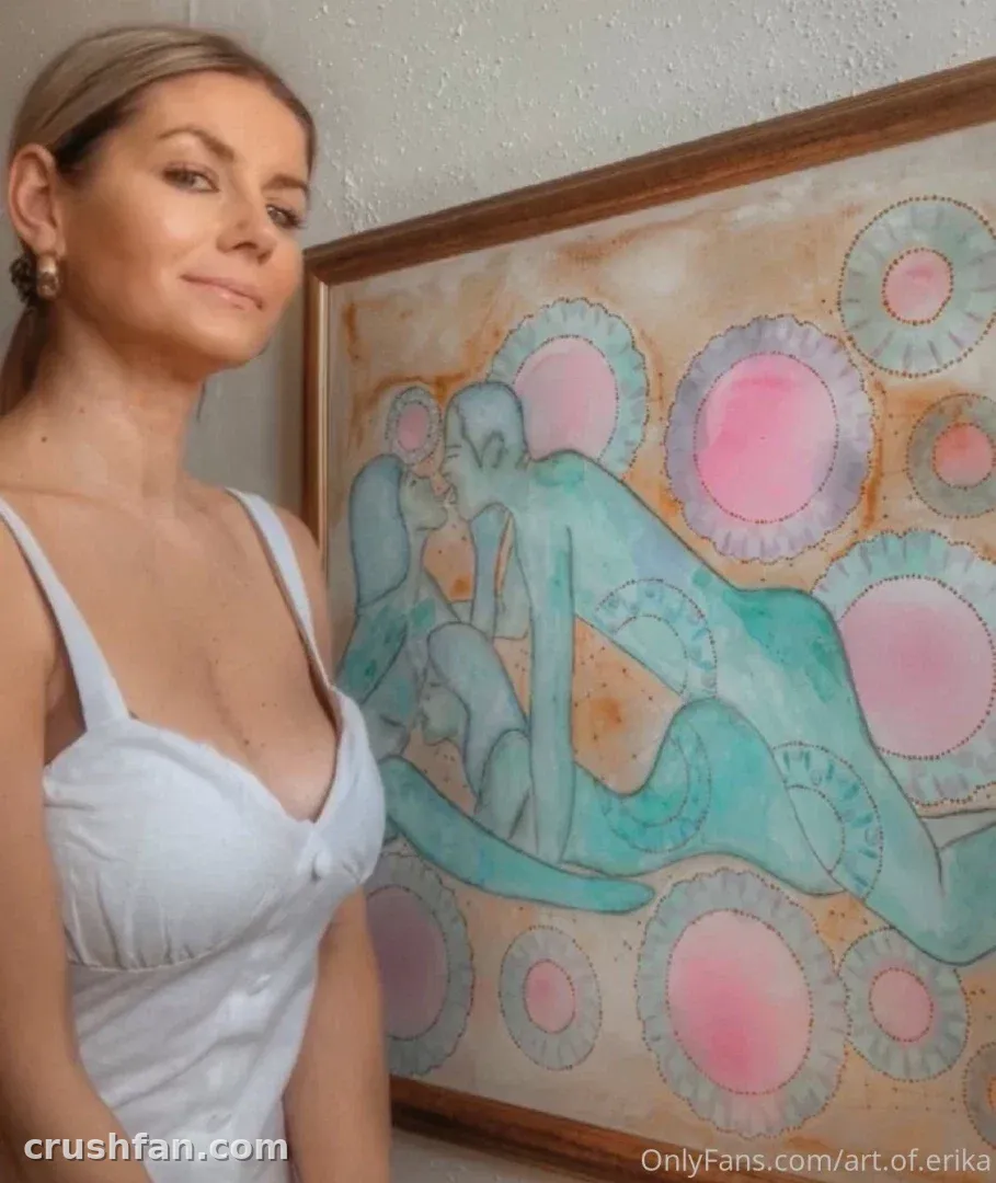 Bad Ery en haut blanc debout près d'une peinture encadrée avec des motifs circulaires roses