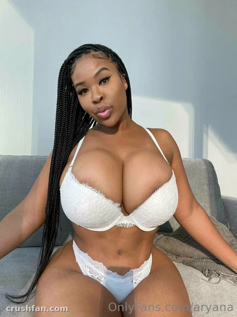 Aryana in white lace lingerie seated on a grey sofa against a light wall