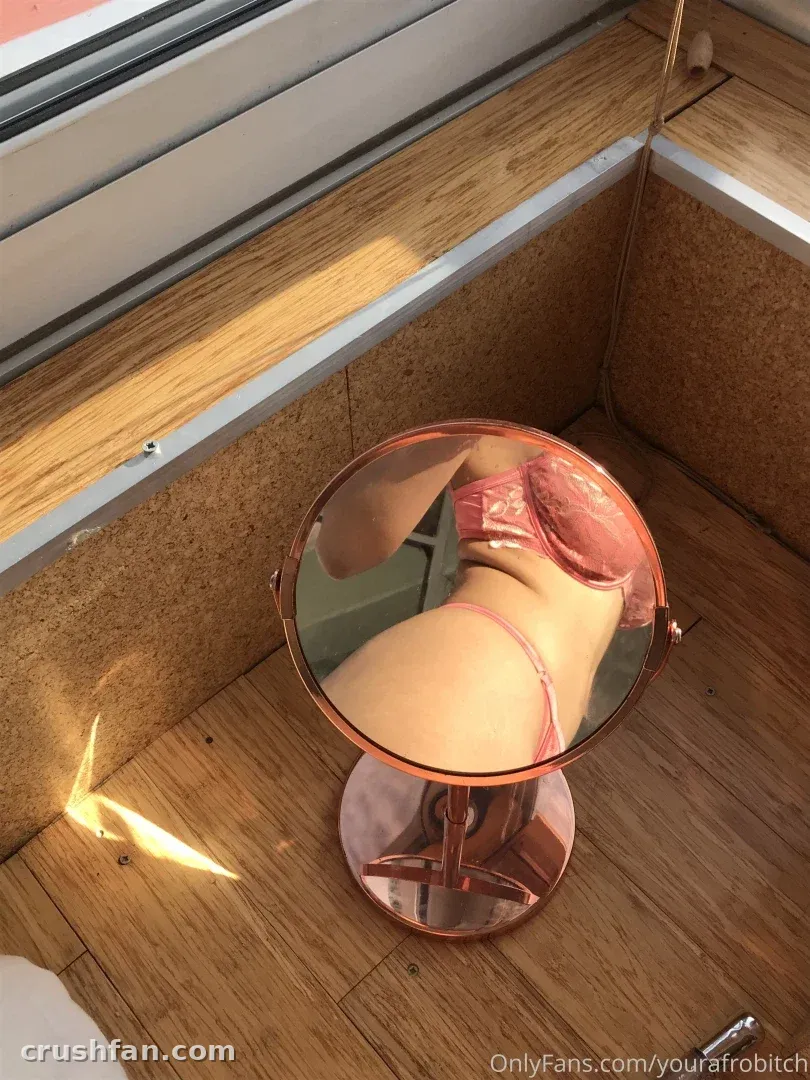 Melissa Ngcobo in pink lingerie reflected in a round mirror on a wooden floor