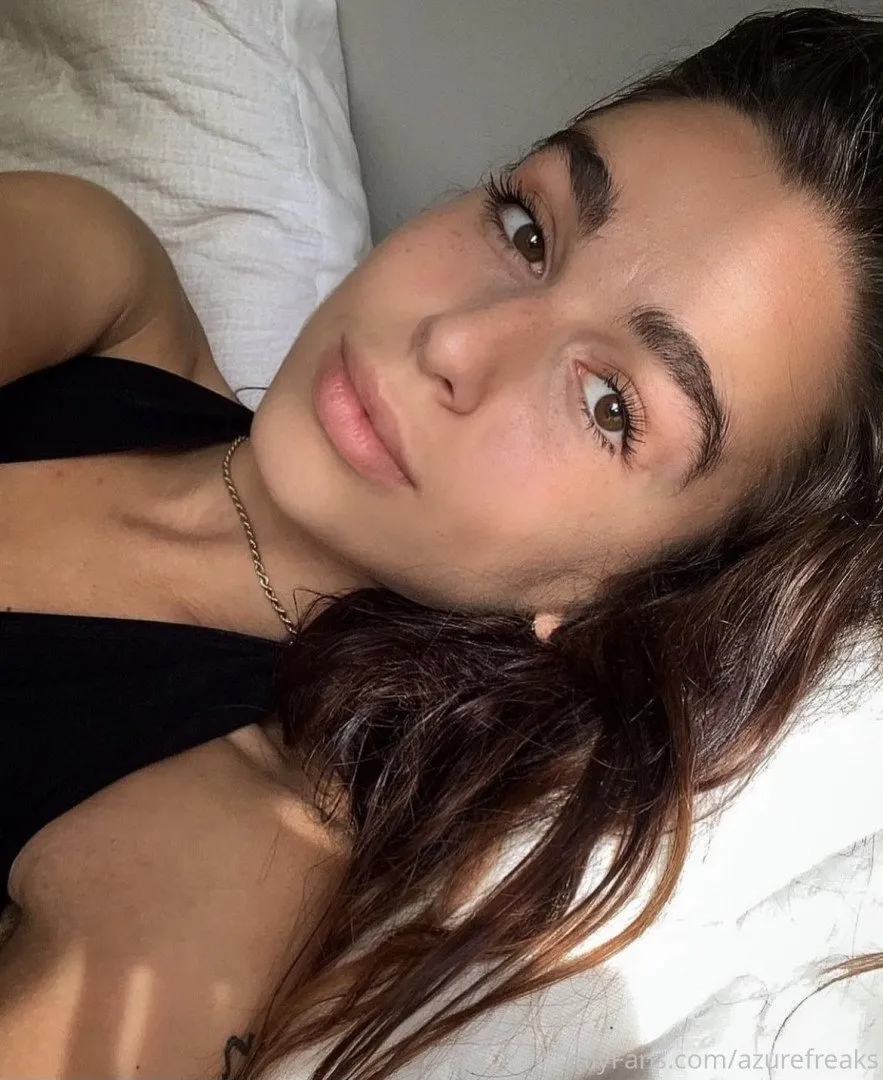 Azure com uma blusa preta deitada sobre roupa de cama branca sob luz natural suave