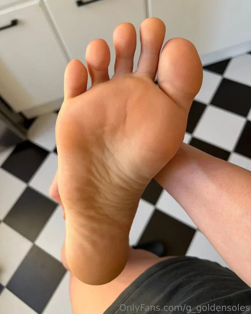 Close-up of a bare sole held toward the camera above a black and white checkered floor.