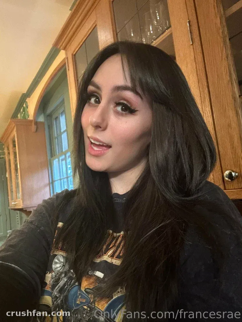 Frances Rae in a kitchen with wooden cabinets, wearing a dark graphic top