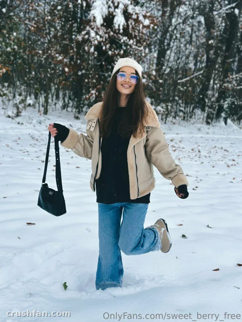 Sweet Berry smiling in a snowy forest wearing a cream jacket and white beanie.