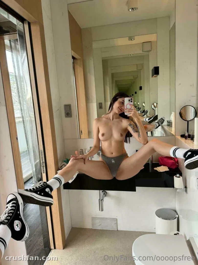 oooops__free macht ein Spiegel-Selfie, während sie in Sneakern und Socken auf einer Badezimmerablage sitzt.