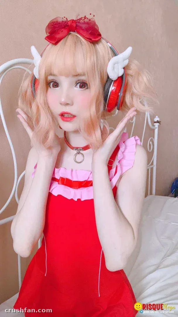 Alisa in a red frilled top and winged headphones posing with hands raised indoors