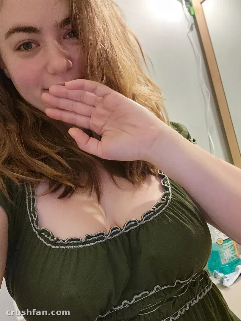 AwesomeKate dans un haut vert levant une main près de son visage à l'intérieur