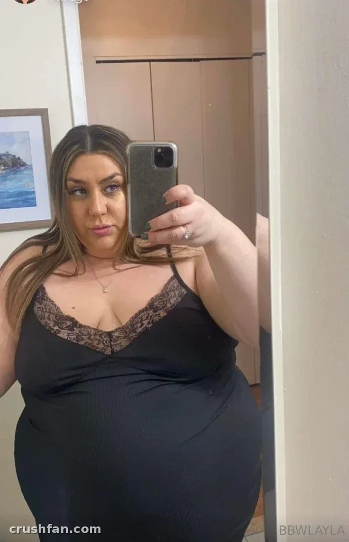BBW Layla in a black lace-trim top taking a mirror selfie indoors.