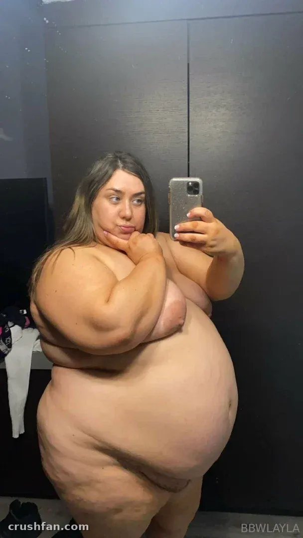 BBW Layla делает селфи в зеркале в слабо освещённой комнате с тёмными панелями позади неё.