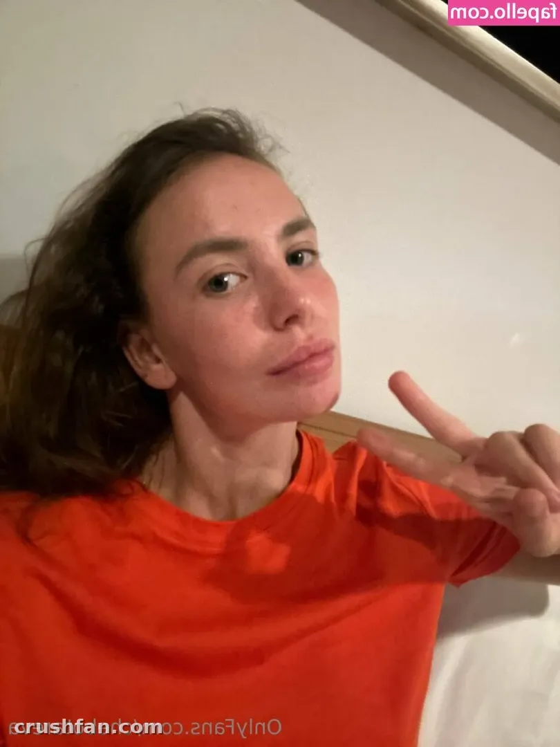 Chebyjane🍑🍒 in an orange top making a peace sign in a close-up indoor selfie.