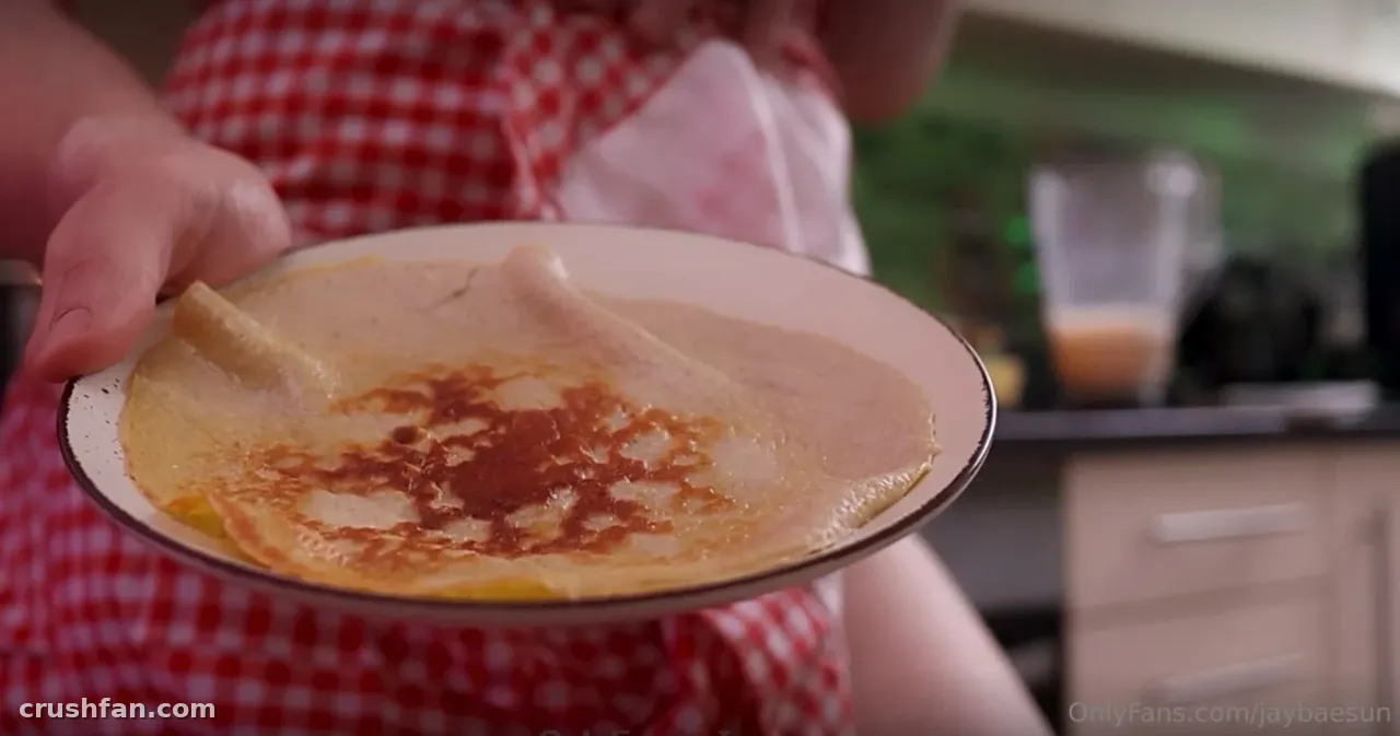 Jaybaesun holding a plate with a folded crepe topped with dark syrup in a kitchen.